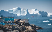 Aerial View of Arctic city of Ilulissat, Greenland. Colorful houses in the center of the town with icebergs in the background in summer on a sunny day with blue sky and clouds. Photo taken in Greenland.